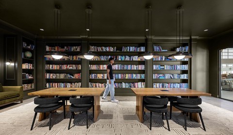 A man is standing in a library with a table and chairs in the foreground.