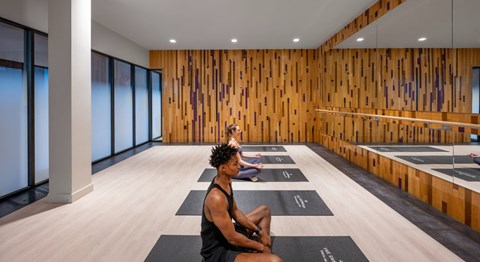 A man is sitting on a yoga mat in a room with wooden walls.