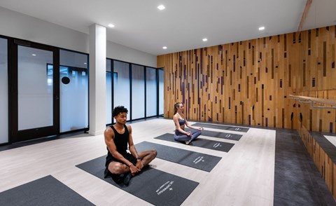 Two people are sitting on yoga mats in a room with wooden walls.