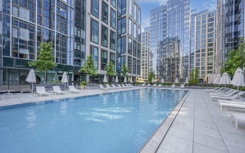 an outdoor swimming pool with chaise lounge chairs and trees in front of a tall building