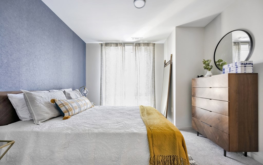 Model bedroom with floor to ceiling window, blue fabric accent wall, and modern decor