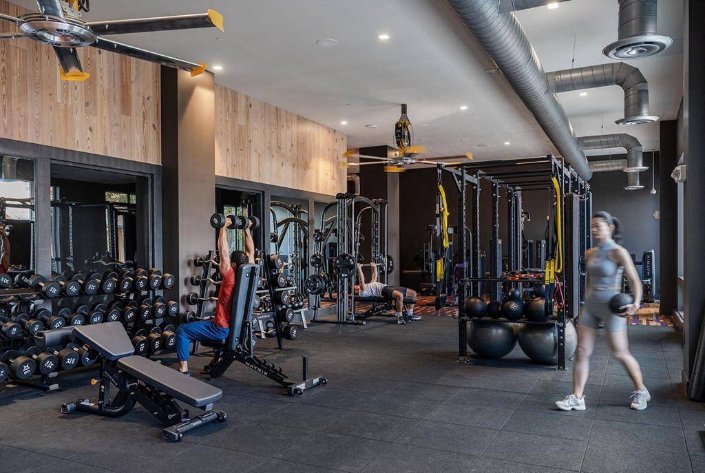 a woman walking through a gym filled with weights and cardio equipment