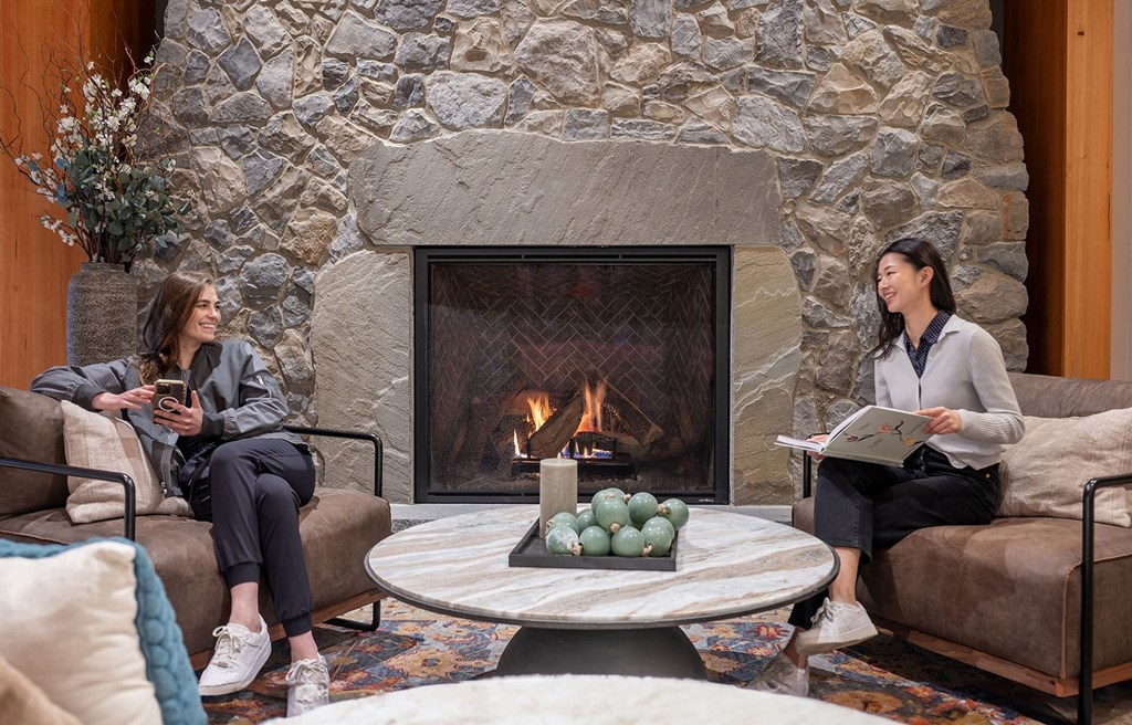 two women sitting on couches in front of a fireplace