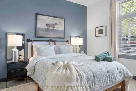 A bedroom with a bed, two lamps, and a painting of a horse.