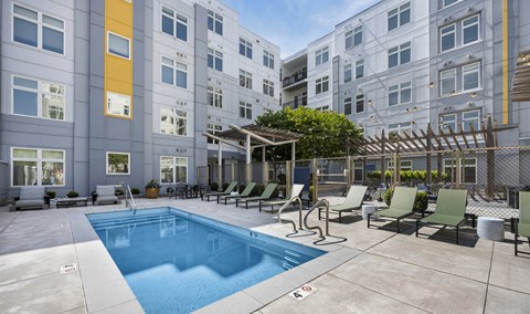 A swimming pool surrounded by chairs and a building in the background.