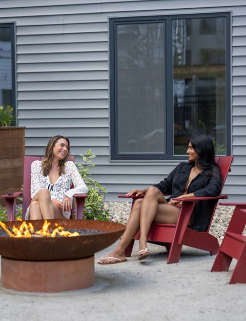 Two women sitting on chairs by a fire pit.