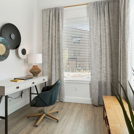 A room with a desk, chair, and curtains.