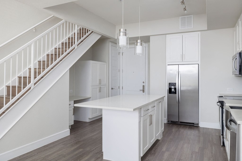 a white kitchen with a white island and a stainless steel refrigerator