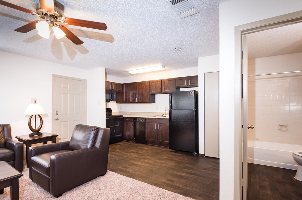 a living room with a ceiling fan and a kitchen in the background