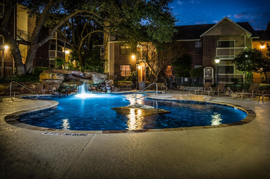 a pool with a waterfall and water feature at night