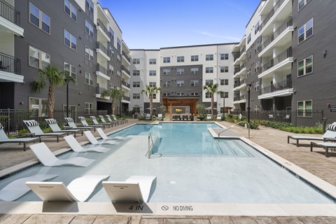 A pool surrounded by lounge chairs and apartment buildings. at Alta Sunset Heights, Houston, 77009