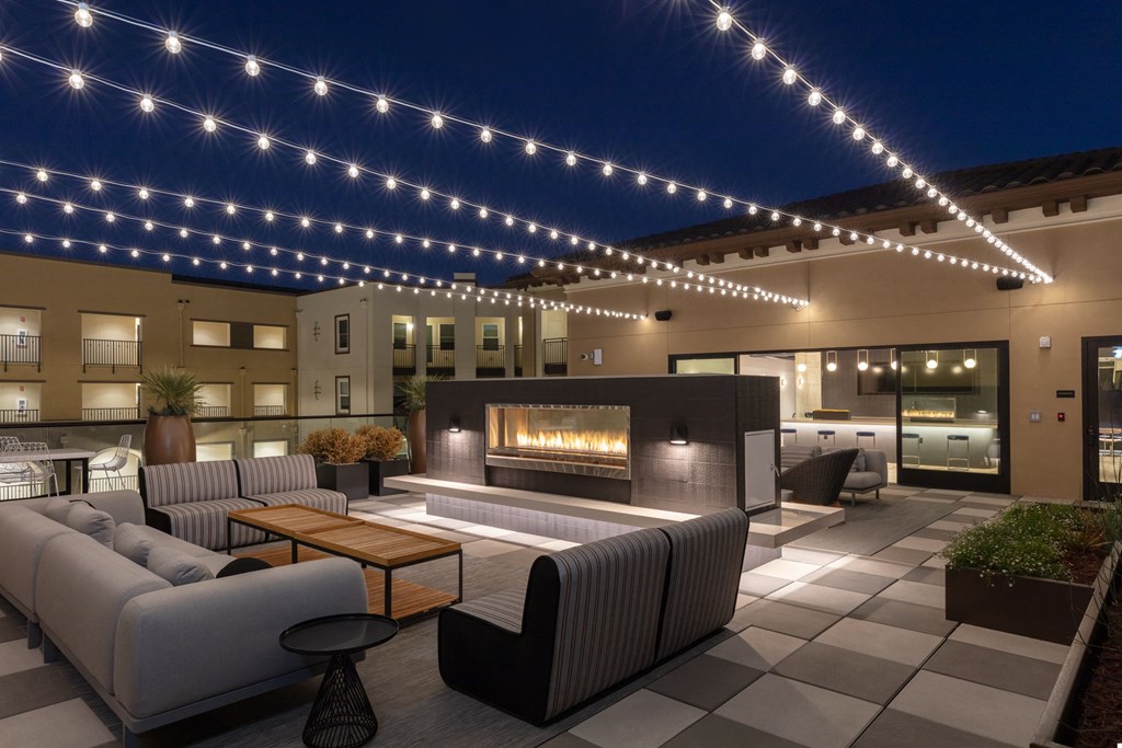 a patio with couches and a fireplace under string lights