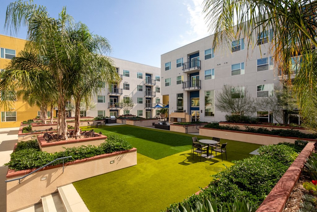 lush outdoor green space with seating and palm trees at Aston at Gateway apartments in El Monte, California