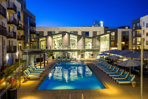 A swimming pool surrounded by lounge chairs and umbrellas at night.