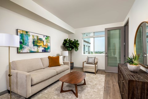 A living room with a beige couch, a wooden coffee table, and a painting on the wall.