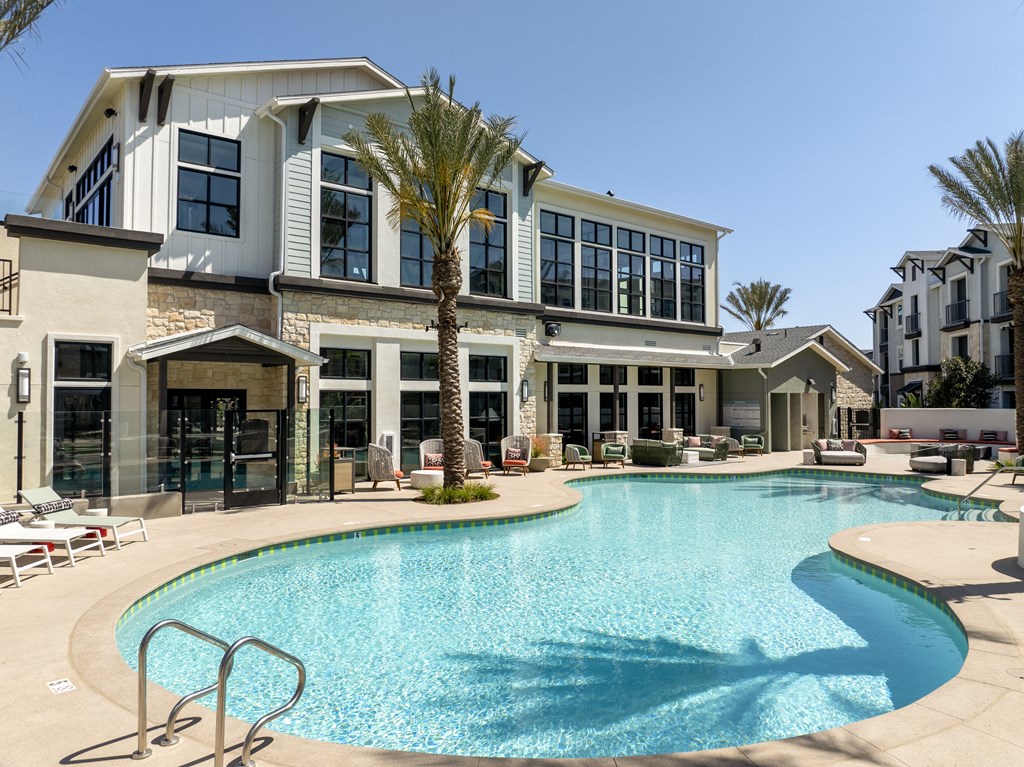 A large swimming pool is in front of a two-story building with a palm tree in front of it.