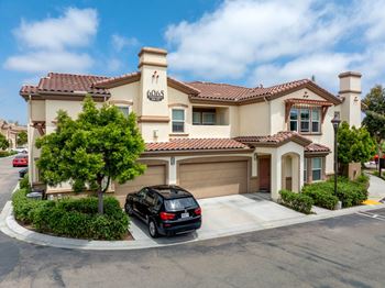 A black car is parked in front of a house with the number 6065 on it.