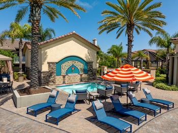 A poolside area with blue lounge chairs and a large orange umbrella.