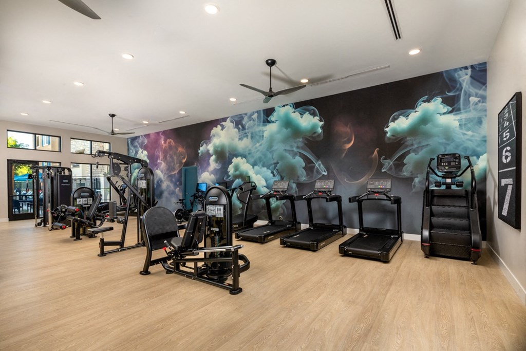 a gym with cardio machines and a wall mural of exercise equipment