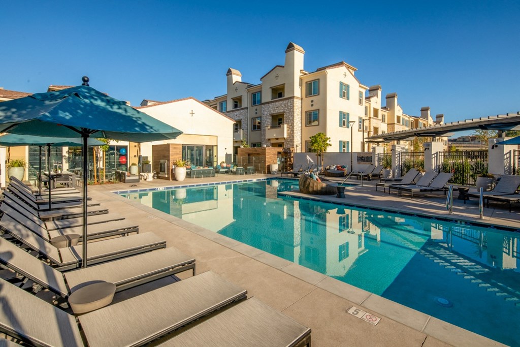 a swimming pool with lounge chairs and umbrellas in front of apartment buildings