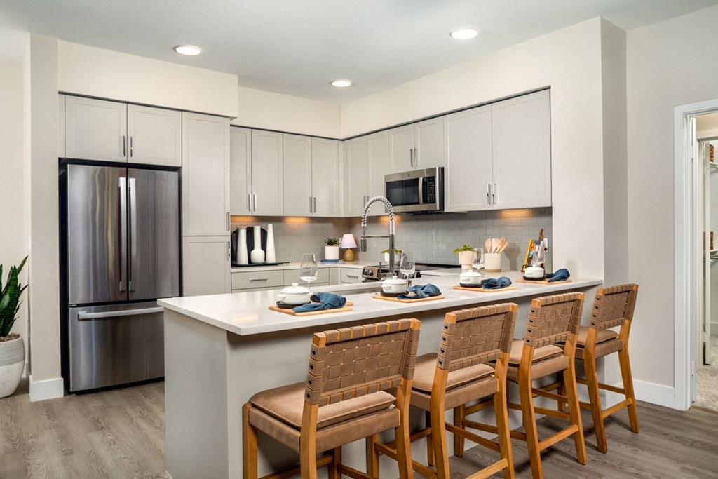 a kitchen with a large island with chairs and a stainless steel refrigerator