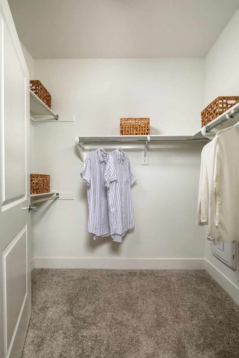 a walk in closet with white walls and shelves and a white closet with clothes hanging
