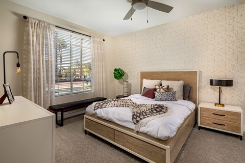 A bedroom with a large bed, a ceiling fan, and a window with blinds.