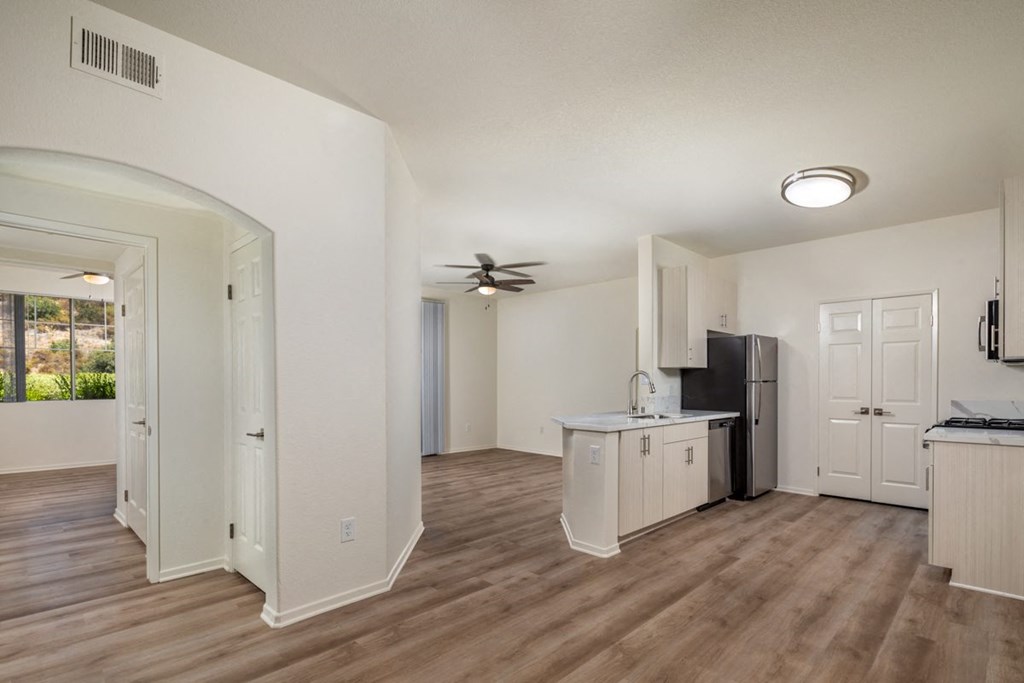 Open living room and kitchen with white walls and wood flooring at Casoleil, San Diego
