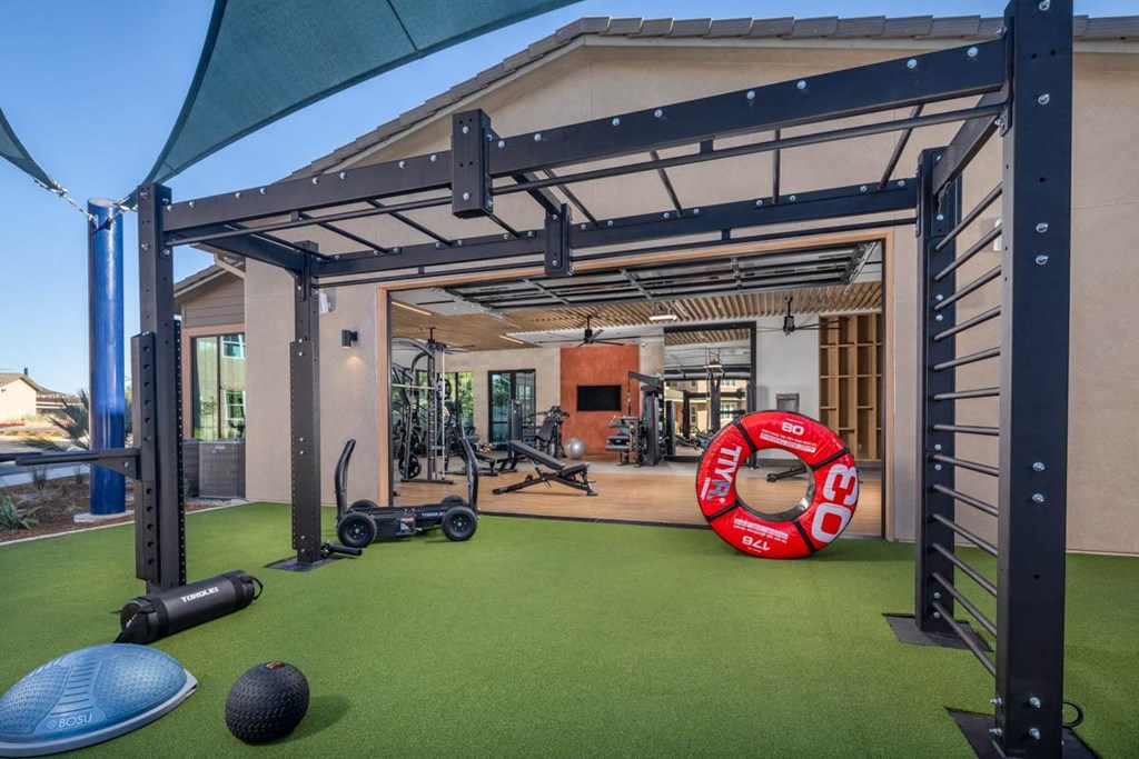 A gym with a green floor and a variety of equipment including a blue exercise ball and a red and white clock.