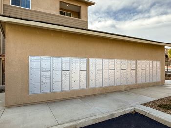 A wall of mailboxes in front of a tan building.