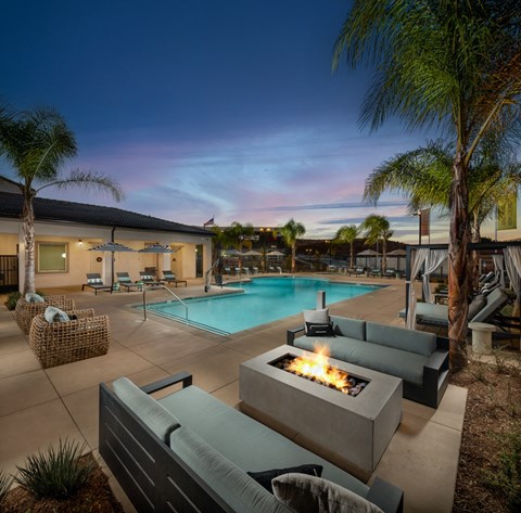 A poolside area with a lit fire pit and lounge chairs.