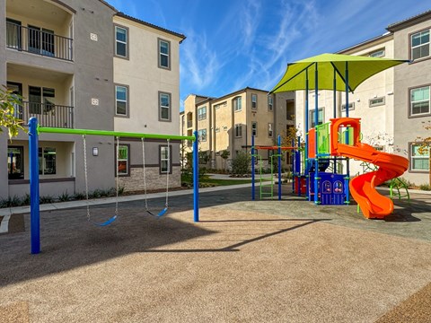 A playground with a slide and swings in front of apartment buildings.