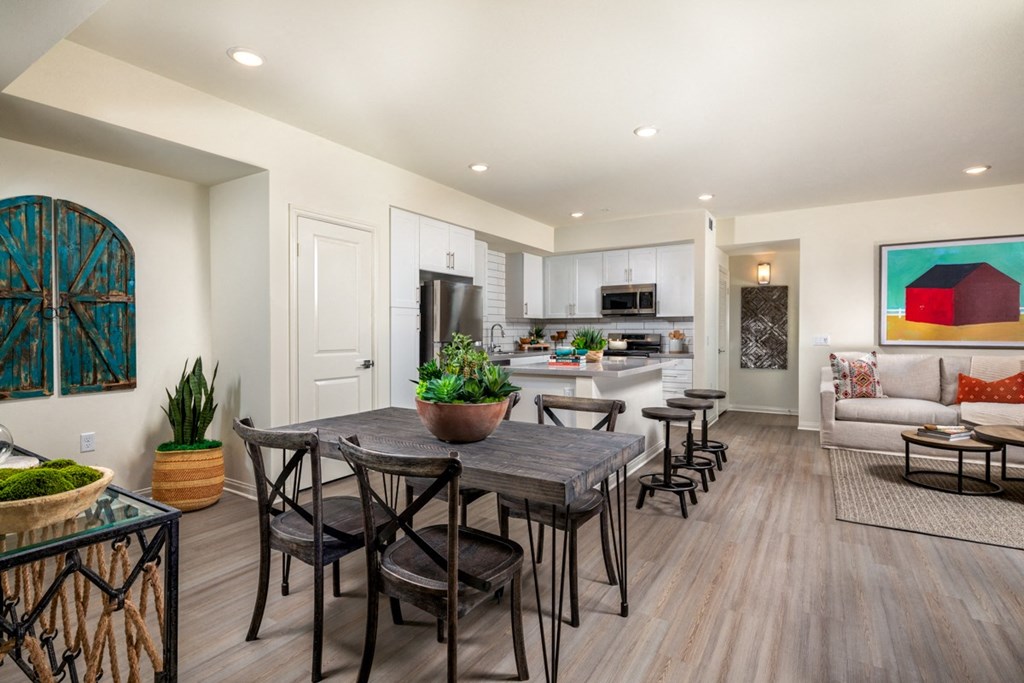 a dining area with a wooden table and chairs and a kitchen in the background