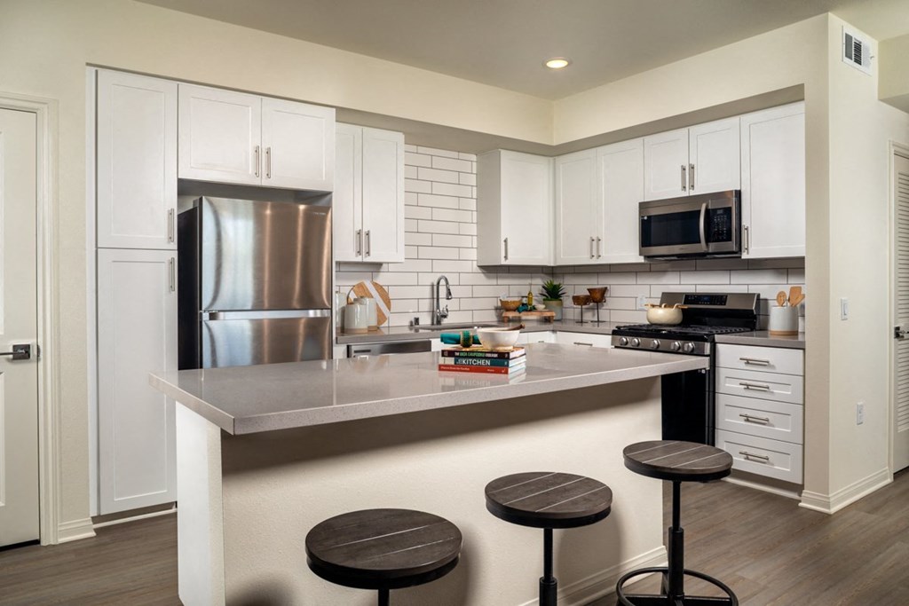 a kitchen with white cabinets and a large island with three stools