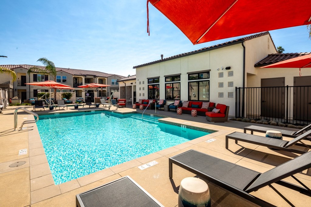 a swimming pool with lounge chairs and umbrellas in front of a building