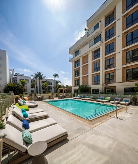 A pool surrounded by lounge chairs with a building in the background.