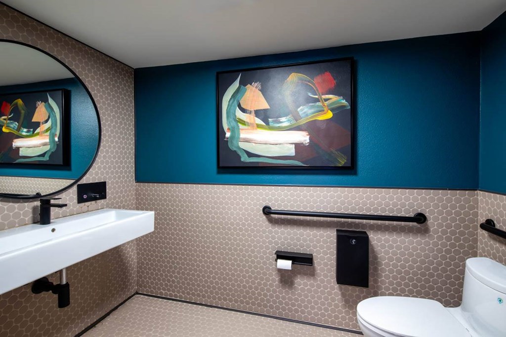 A bathroom with a toilet, sink, and a painting on the wall.