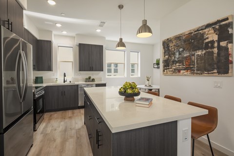 A modern kitchen with a large island and a refrigerator on the left.