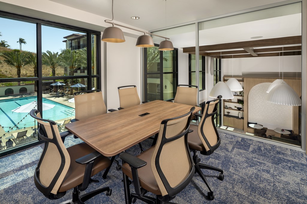 A conference room with a long table and chairs with a view of the pool and outdoors.