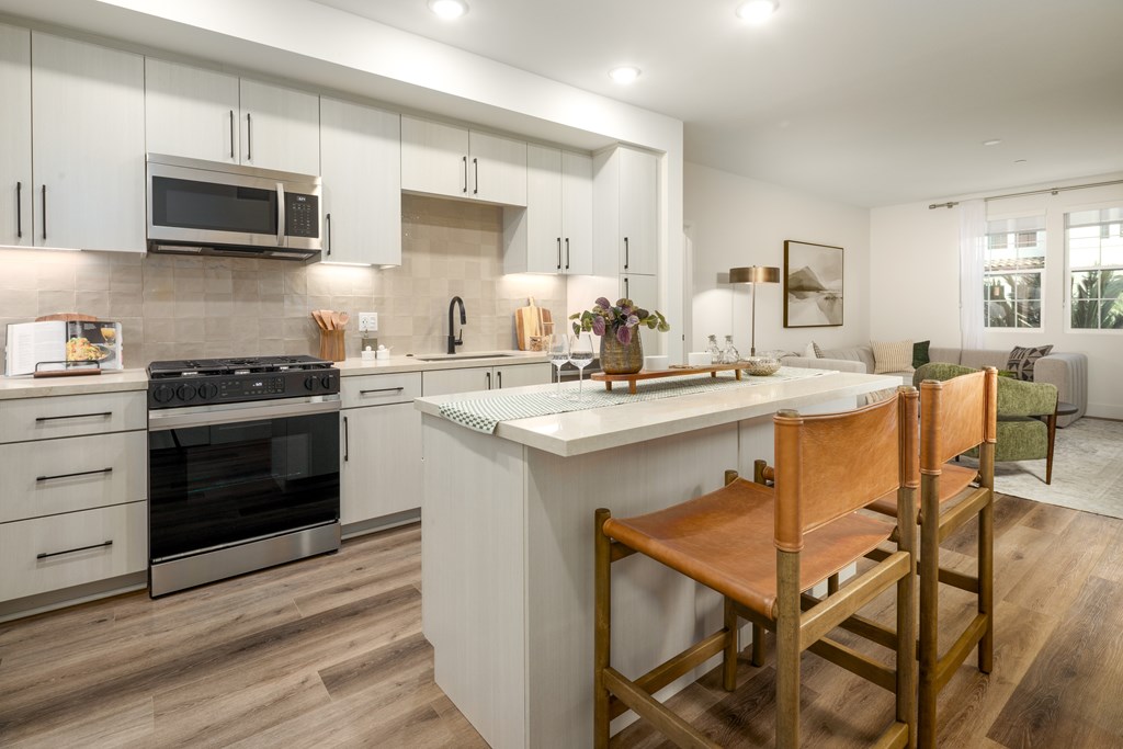 A modern kitchen with a white island and wooden chairs.
