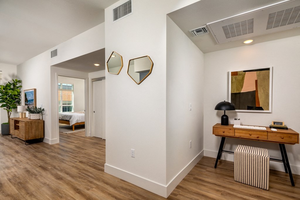 a living room with white walls and wood flooring and a desk and a window