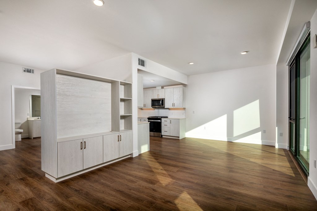 a living room with white walls and a kitchen with a wood floor