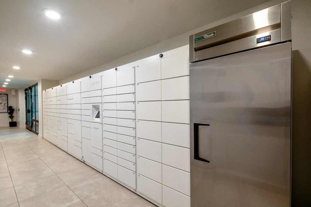 a set of white lockers in a hallway with a stainless steel refrigerator