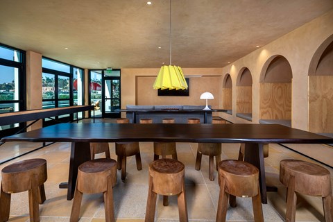 A long wooden table with matching chairs is in the middle of a room with a yellow lamp hanging from the ceiling.