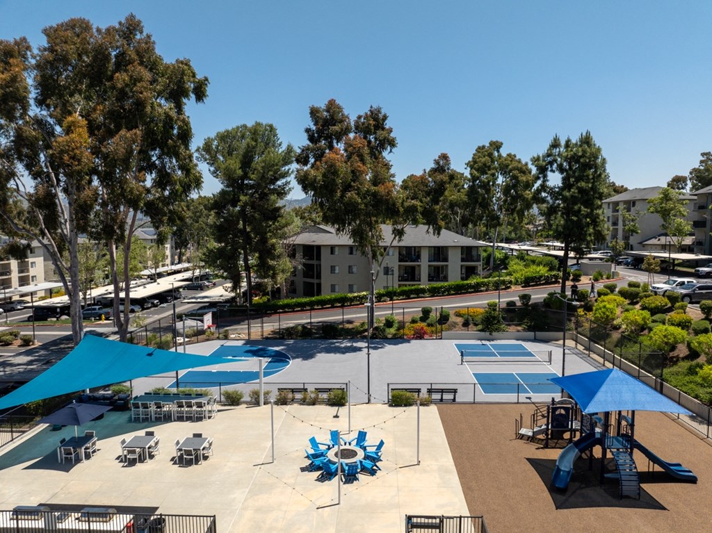 an aerial view of an a tennis court and basketball court with blue umbrellas and tables and playground