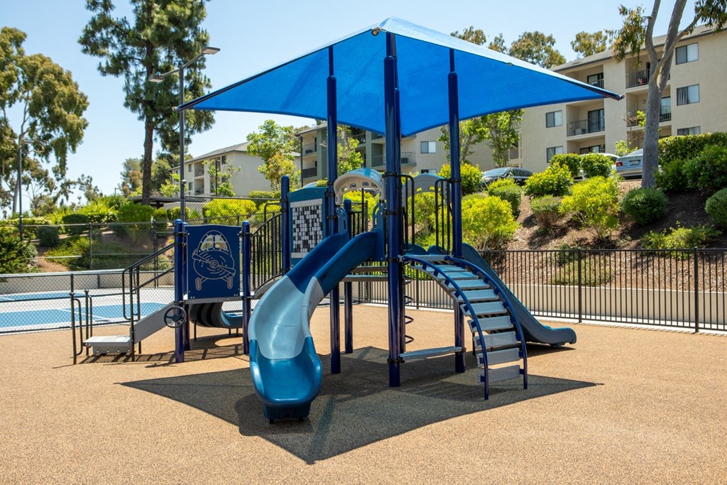 a playground with a blue slide and umbrella