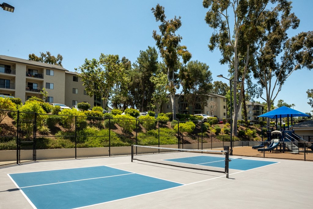 a tennis court with apartments and a playground in the background