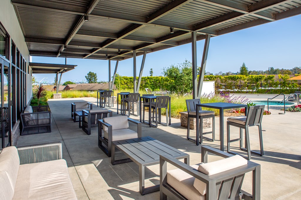 a patio with tables and chairs and a pool in the background