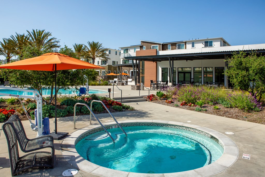 a jacuzzi pool with chairs and an umbrella in front of a building