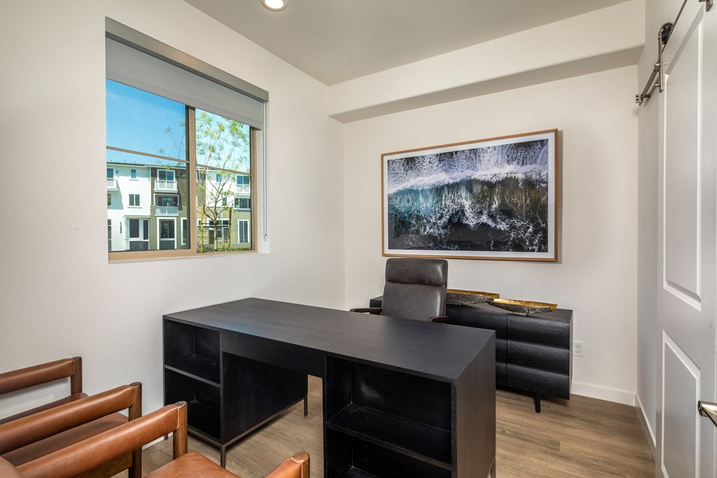a room with a desk and chairs and window